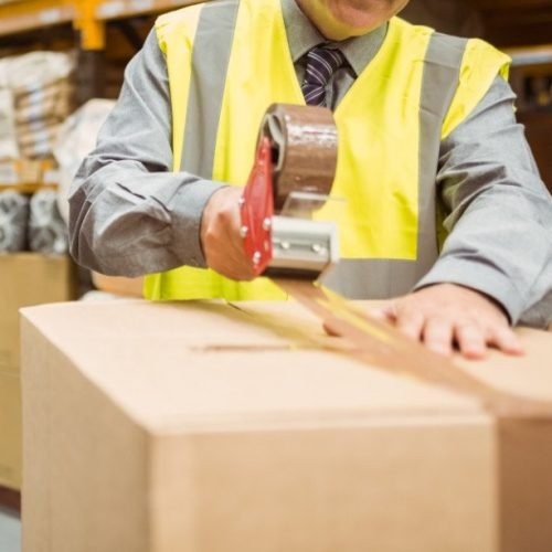 Warehouse worker sealing cardboard boxes for shipping in a large warehouse